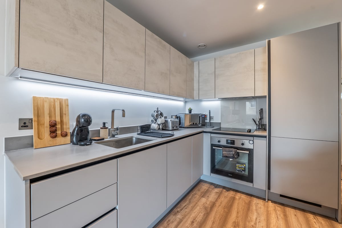 Kitchen at the Aspire apartment with light grey cabinets, stainless steel appliances, white countertops and wooden flooring