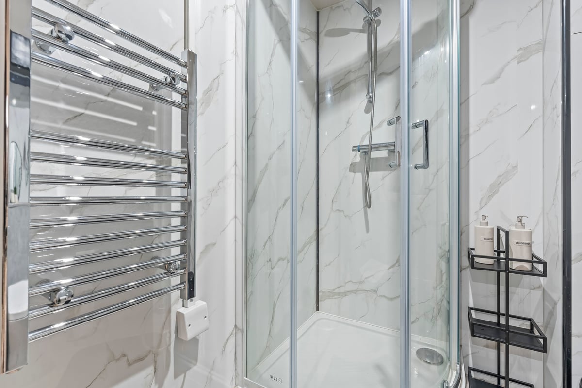 Modern bathroom at Athenaeum House with white marble walls, a frameless glass shower enclosure and a chrome towel radiator on the left wall