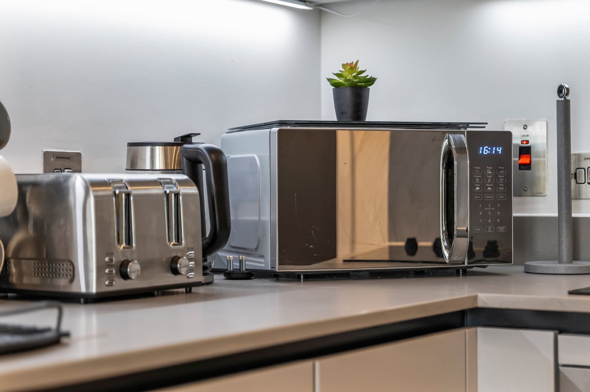 Kitchen counter at the Aspire apartment with stainless steel appliances including a toaster, microwave and coffee maker, with a small potted plant on top