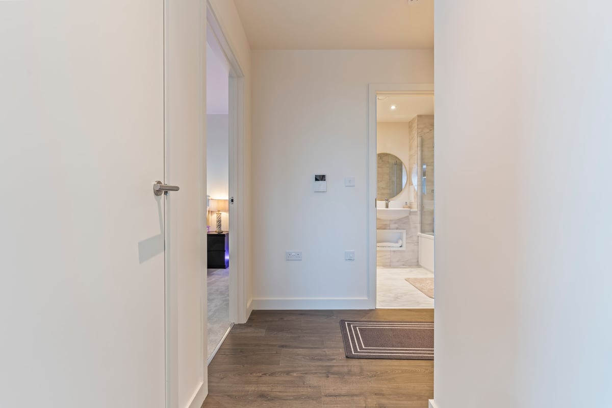 Hallway at Wedgewood with white walls and wooden flooring, with the doorway leading into a bathroom where the floating vanity is visible
