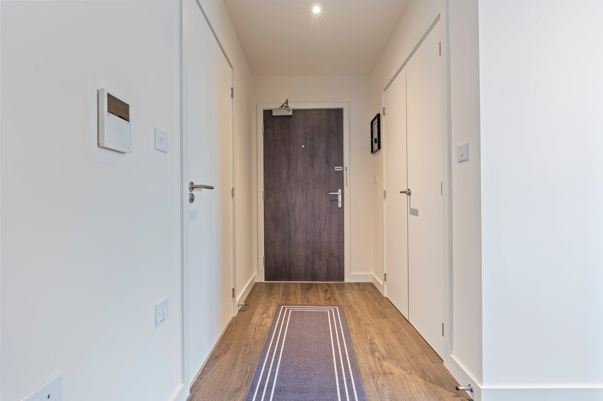 Hallway at Wedgewood with white walls, hardwood flooring, a dark wooden front door and a striped runner rug