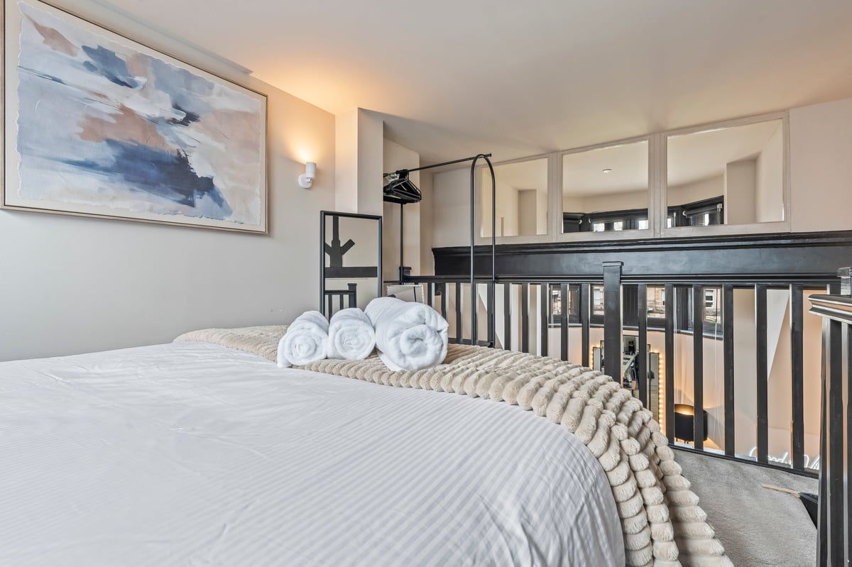 Modern bedroom at Athenaeum House with a queen bed, white linens, rolled towels and an adjacent baby crib with dark wood railing