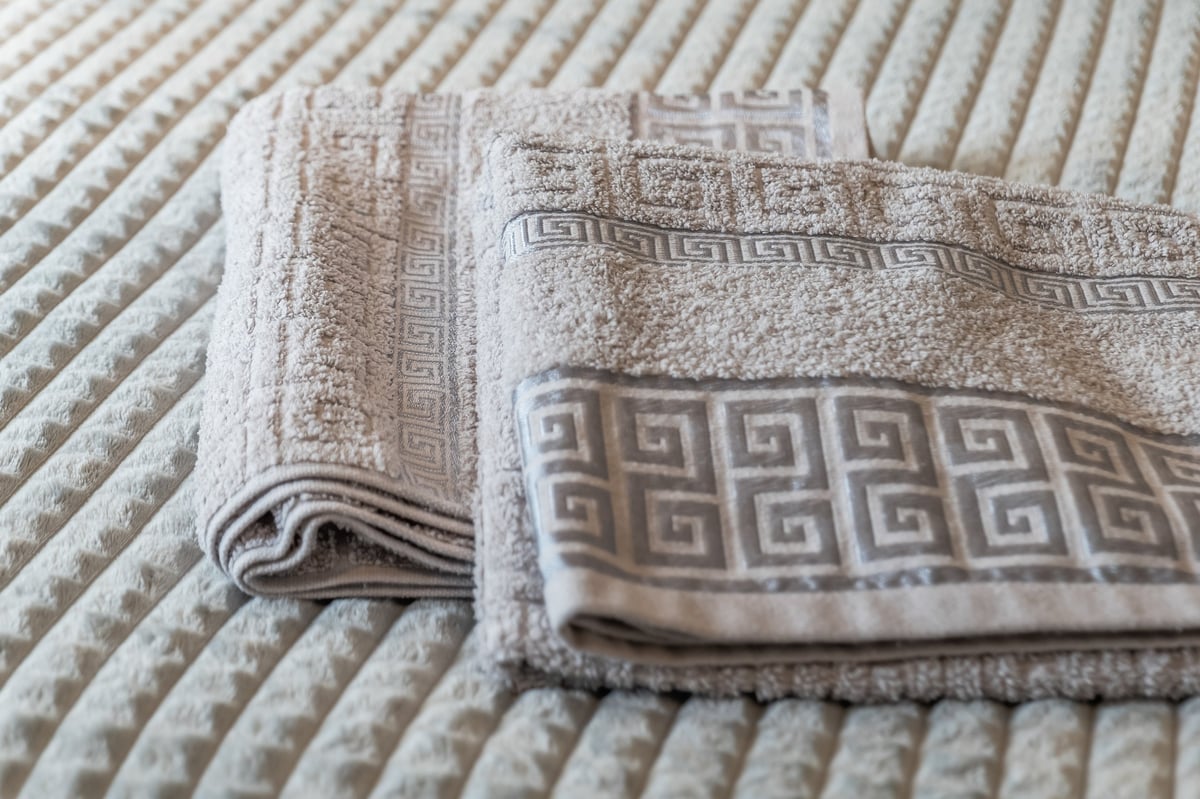 Folded beige towels with a Greek-key pattern at the Aspire apartment, stacked on a textured ribbed surface