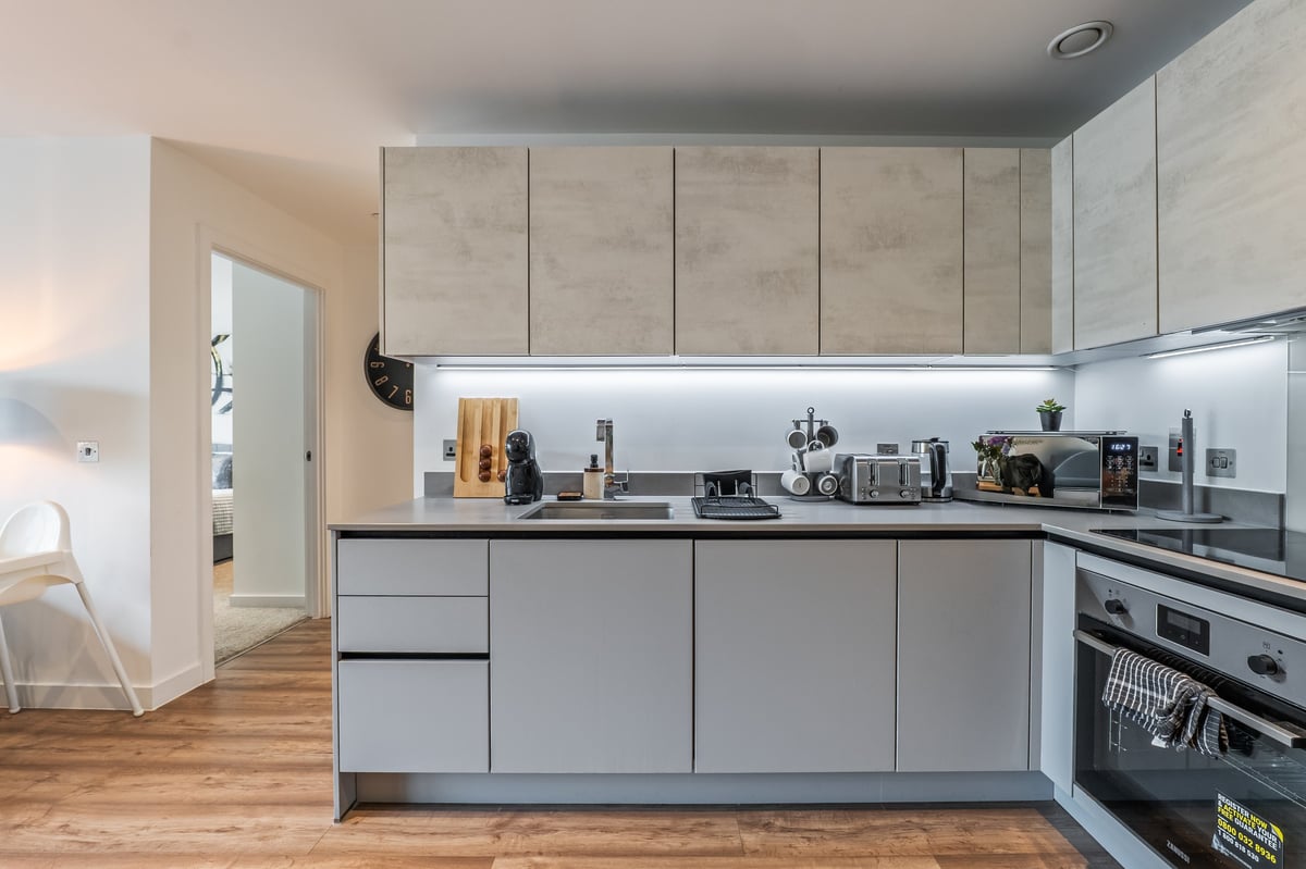 Kitchen at the Aspire apartment with light grey cabinets, white splashback, integrated appliances and wooden flooring