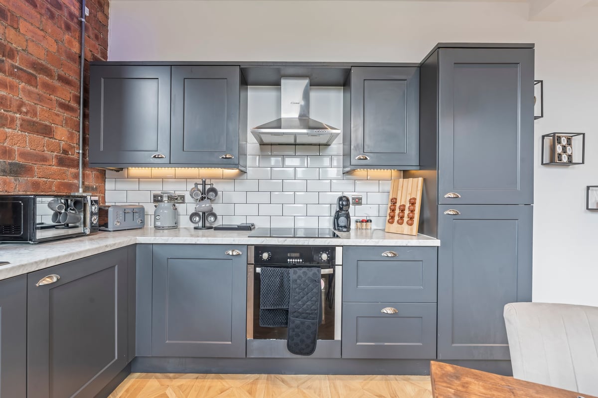 Kitchen at The Calls with grey cabinetry, a white subway tile splashback and a stainless steel range hood