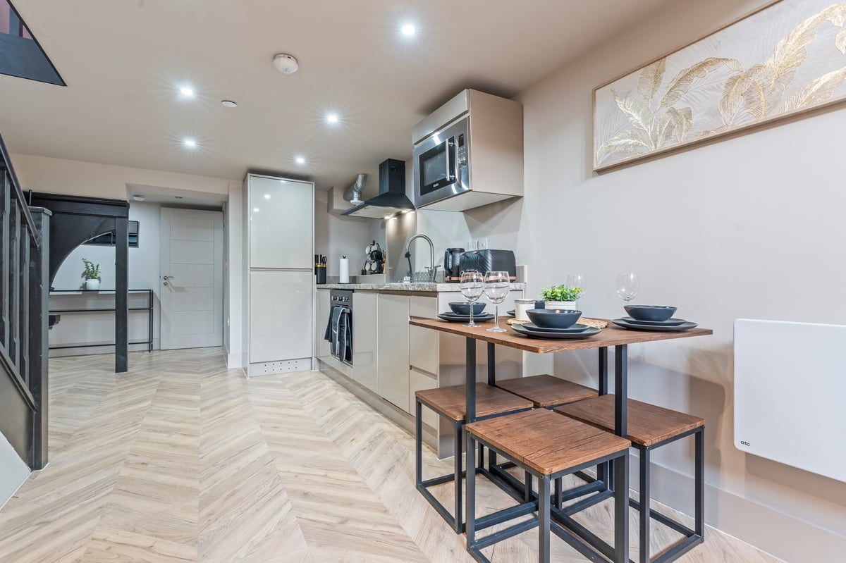 Modern kitchen at Athenaeum House with white cabinetry, a wood dining table with metal-frame chairs, herringbone flooring and stainless steel appliances