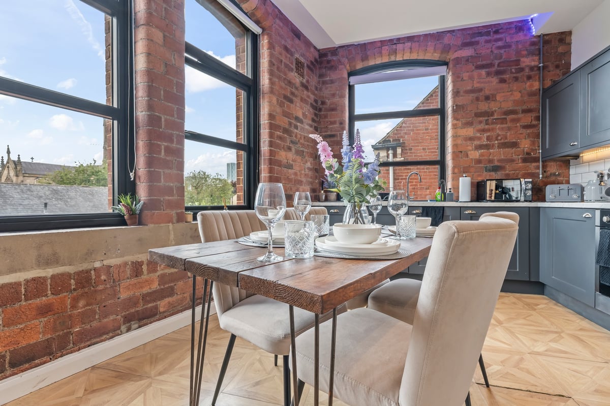 Kitchen and dining area at The Calls with exposed brick, black cabinets, a wooden dining table and large windows