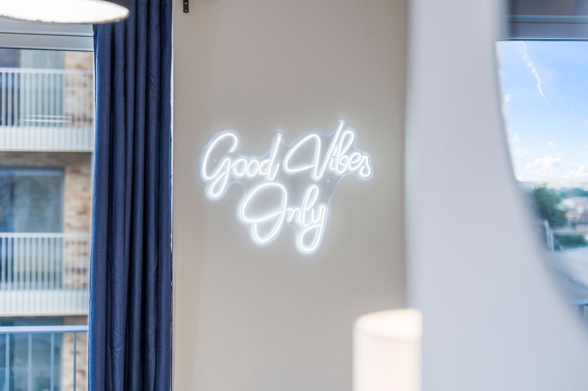 White neon sign reading 'Good Vibes Only' mounted on a beige wall at Wedgewood, between windows with city views