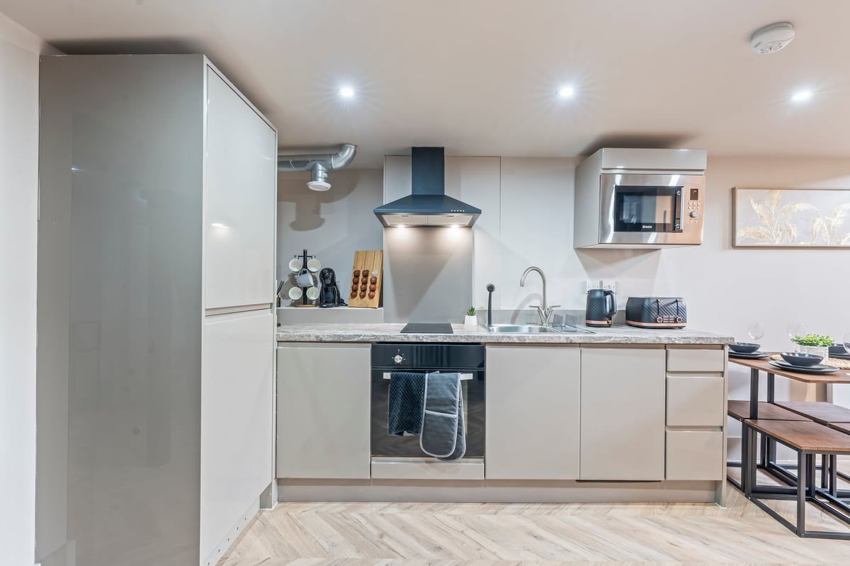 Modern kitchen at Athenaeum House with light cabinetry, stainless steel appliances, a blue range hood and the dining table beyond