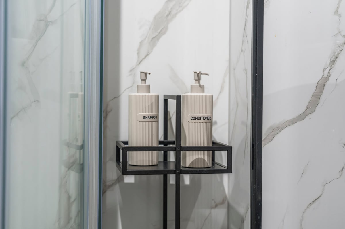 Black metal shelf at Athenaeum House with two beige soap dispensers mounted on the marble-tiled shower wall