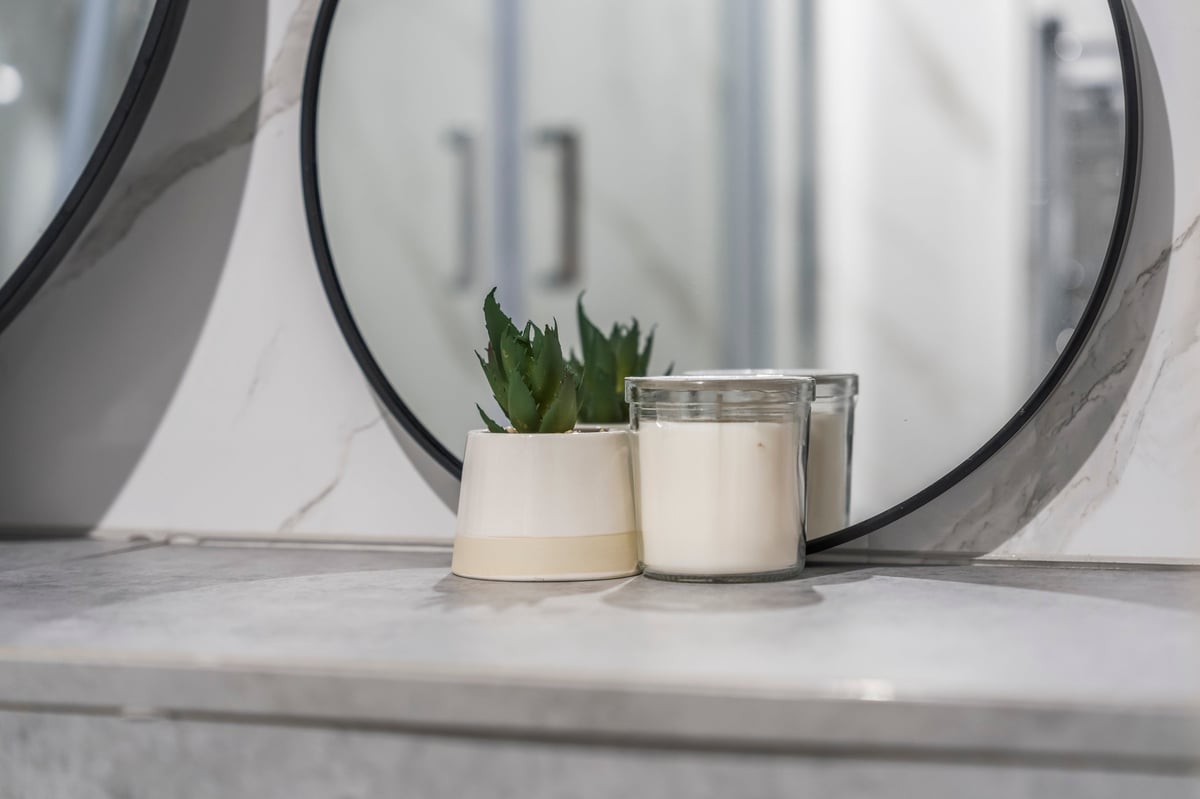 Two white candles and a small succulent plant on the bathroom counter at Athenaeum House in front of a round mirror with a black frame
