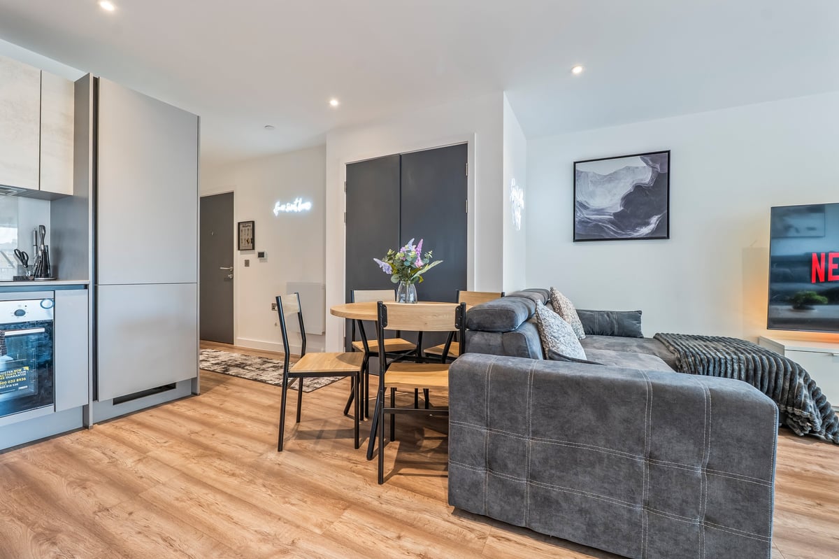 Open-plan apartment interior at the Aspire apartment with a grey sofa, dining table, kitchen, wooden flooring and contemporary artwork on the walls